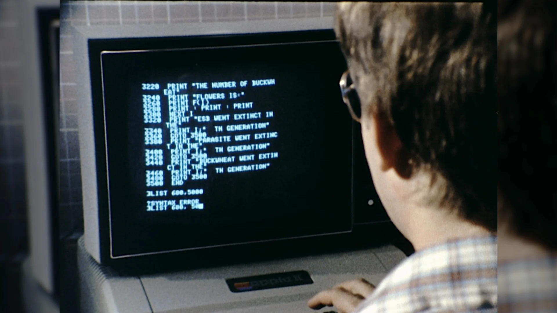 A photo of a man with glasses looking at a computer terminal from the 1990s.